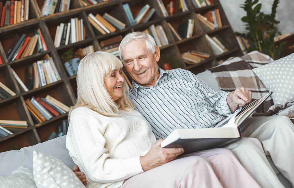 A senior woman and man sitting on a couch and looking at a book together
