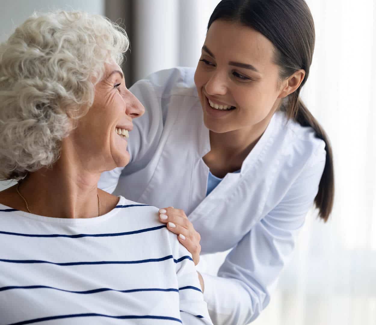 A nurse leaning down to talk to a senior woman seated