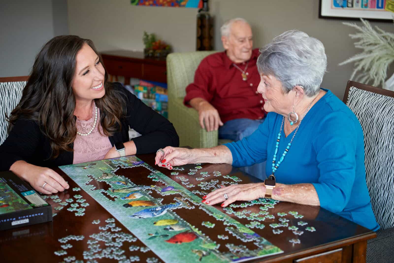 senior woman sitting a table putting a jigsaw puzzle together with young woman