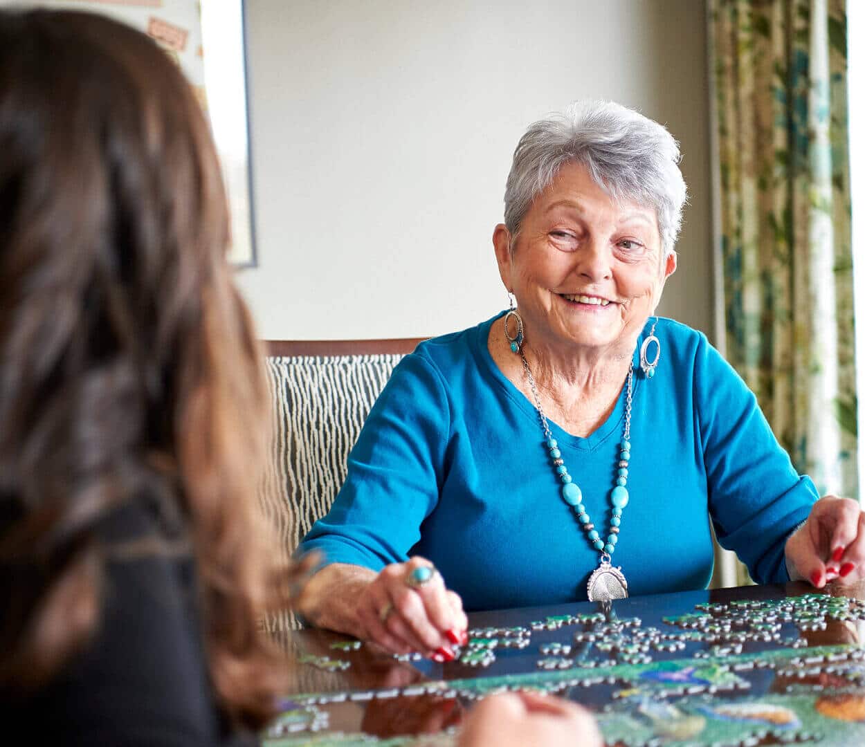 senior woman sitting a table putting a jigsaw puzzle together with young woman