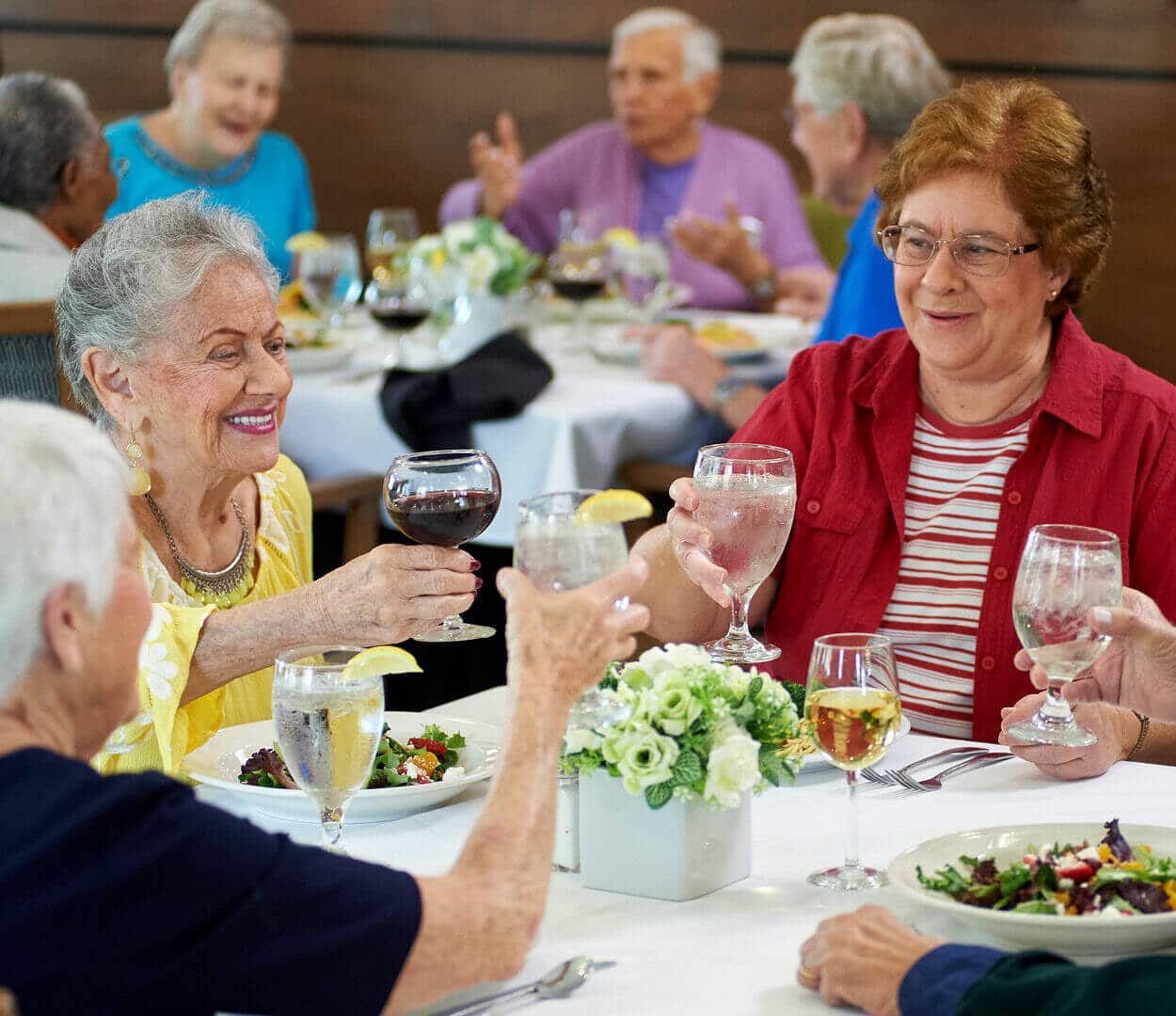 senior residents sitting at dinner with plated food and making a toast with their beverages