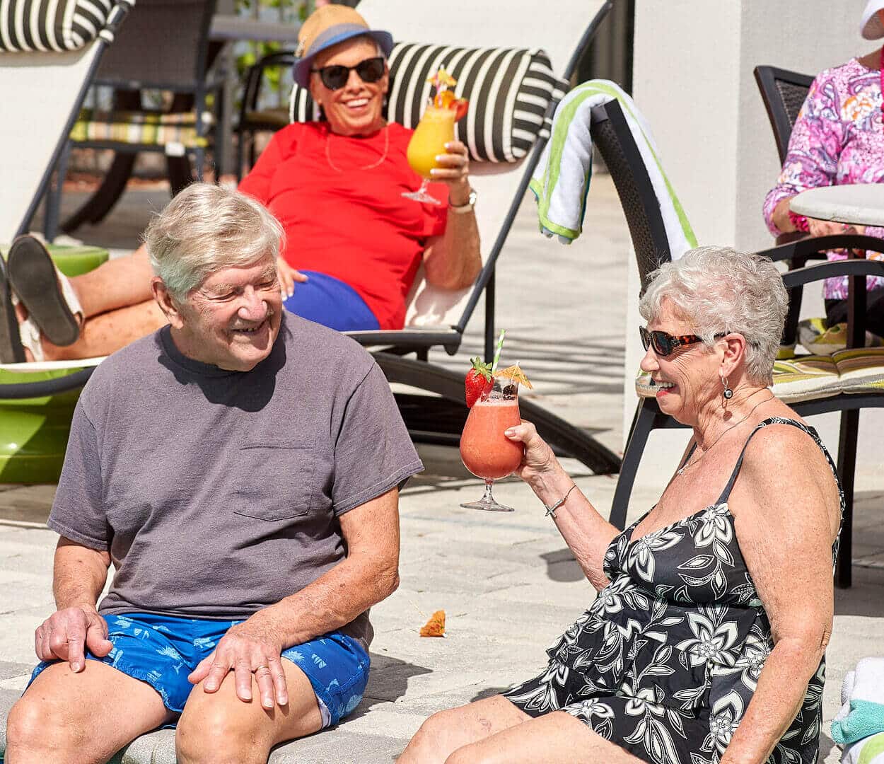 senior men and senior women sitting poolside drinking cocktails