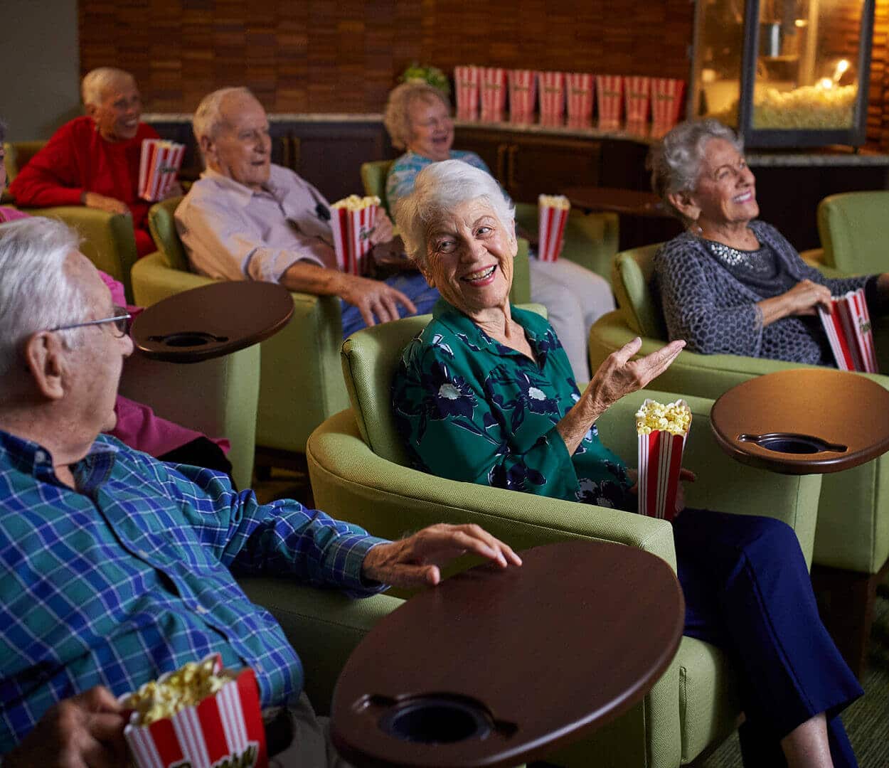 group of senior residents seated in the theater watching a moving and eating popcorn