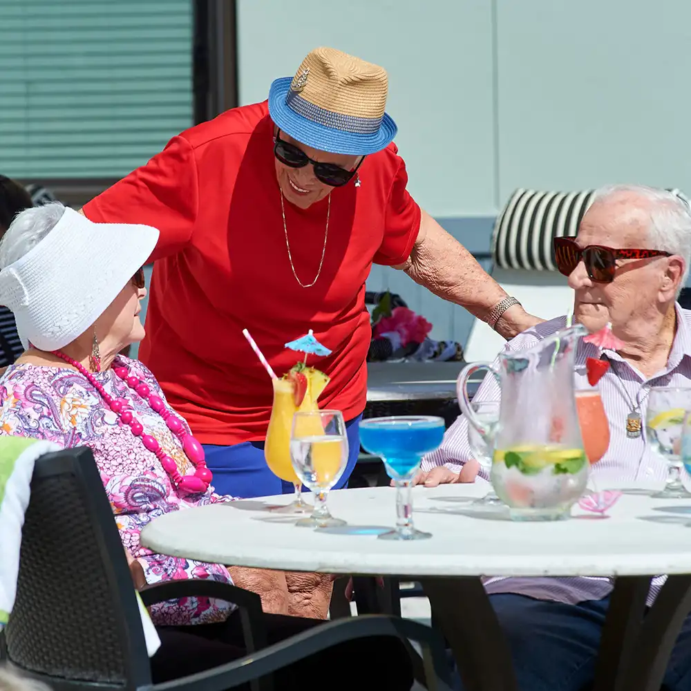 senior woman in red shirt standing over a senior couple seated at the poolside table
